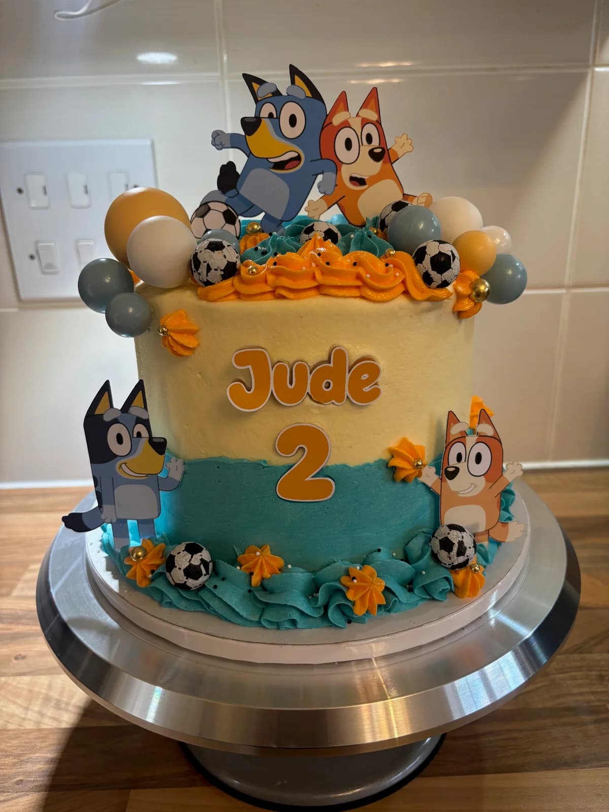 Bluey second birthday cake with blue and orange piping, footballs and character toppers