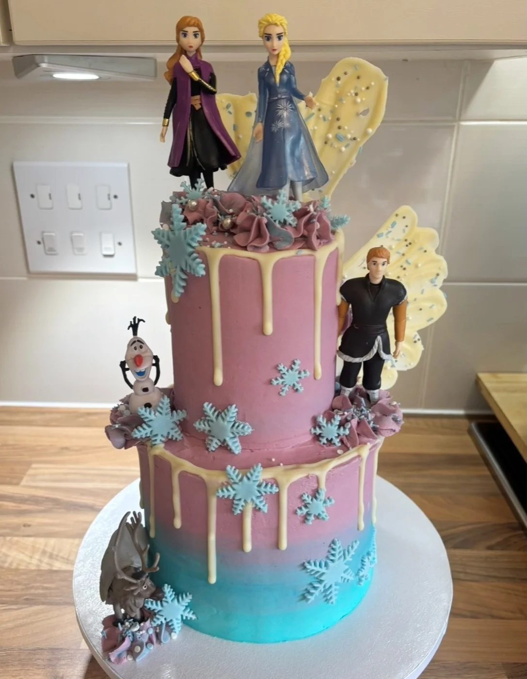 Two tier Frozen birthday cake with pink and blue icing, white chocolate drips and snowflakes